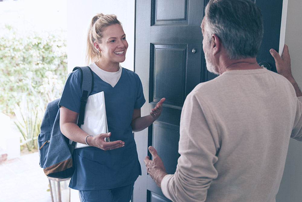 Smiling nurse standing in an open doorway to a patient's home